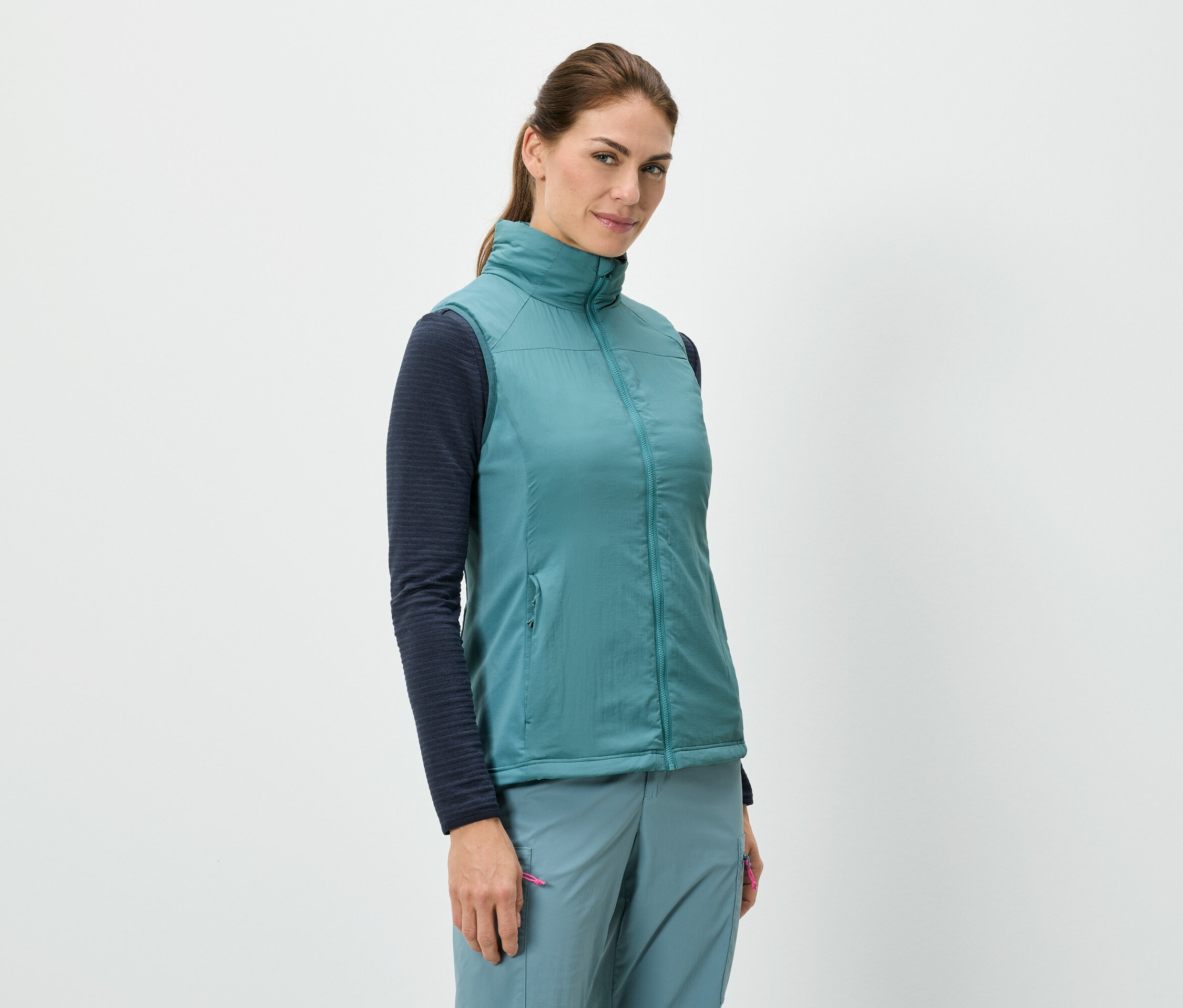 Egy nő áll, és kék mellényt visel egy hosszú ujjú felső fölött, kék nadrággal kombinálva.