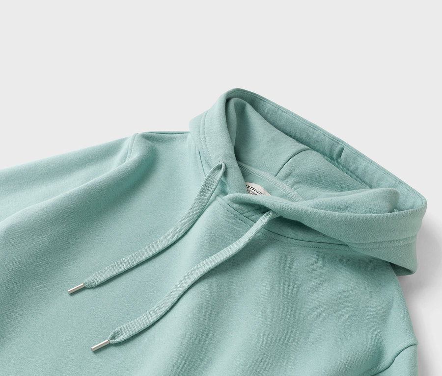 Közelkép egy mentazöld kapucnis pulóverről húzózsinórral.