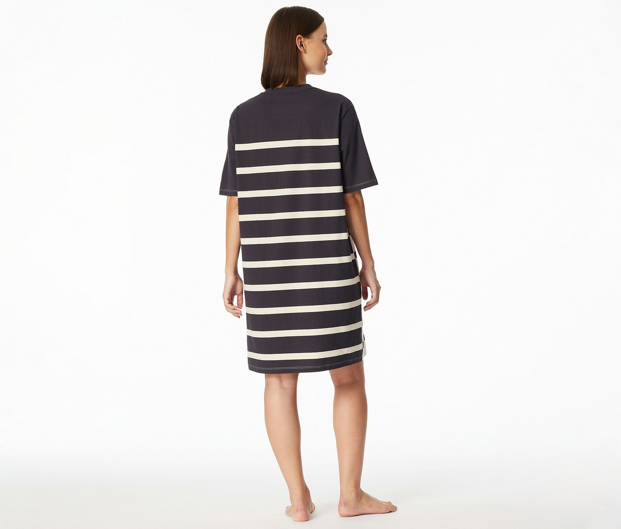 Egy nő mezítláb áll háttal a kamerának, enyhén jobbra néz, és csíkos SCHIESSER hálóinget visel.