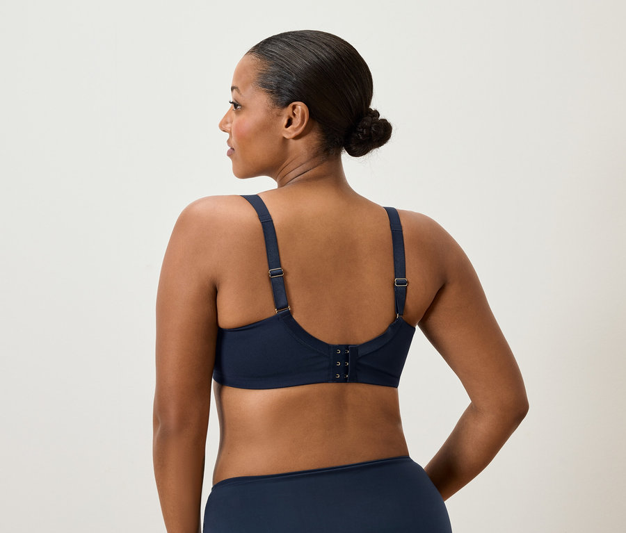 Hátulnézet egy kontyos nőről, aki sötétkék melltartót és alsóneműt visel.