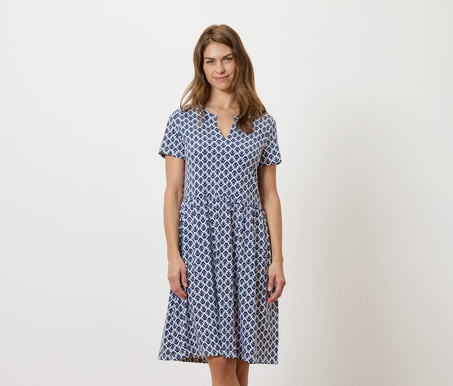 Egy nő áll és kék-fehér ruhát visel.