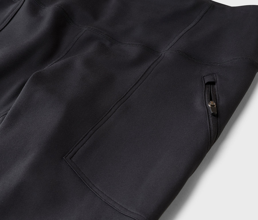 Fekete sportleggings vagy nadrág közelképe, oldalsó cipzáras zsebbel és látható varrásokkal.
