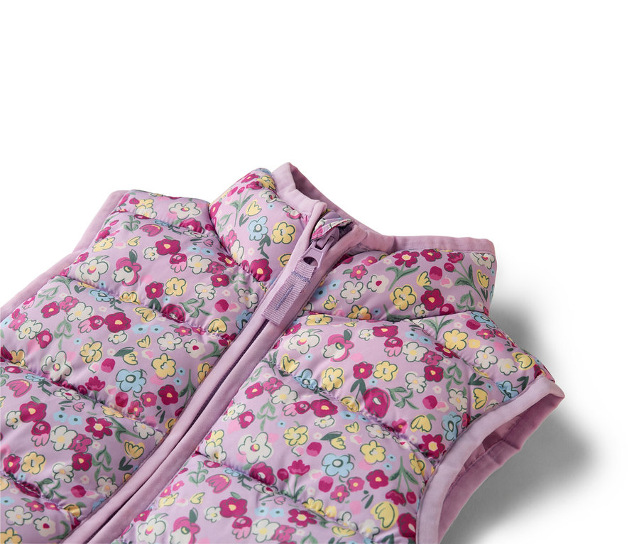 Egy lila, virágmintás, steppelt mellény közeli képe cipzárral.