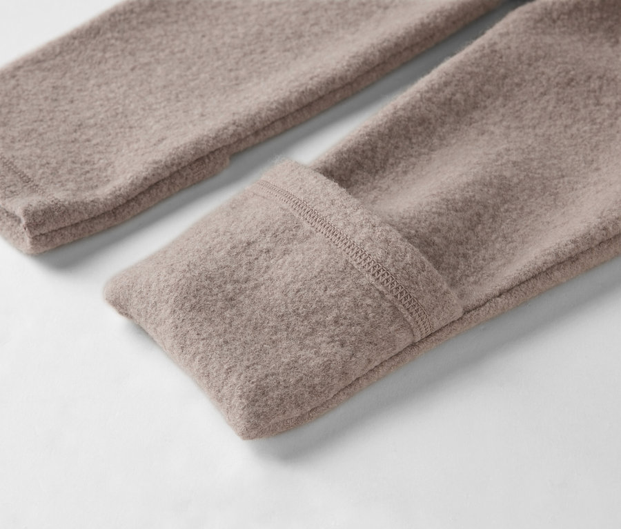 Egy világosbarna gyapjúpulóver két ujjának közeli képe fehér háttéren.