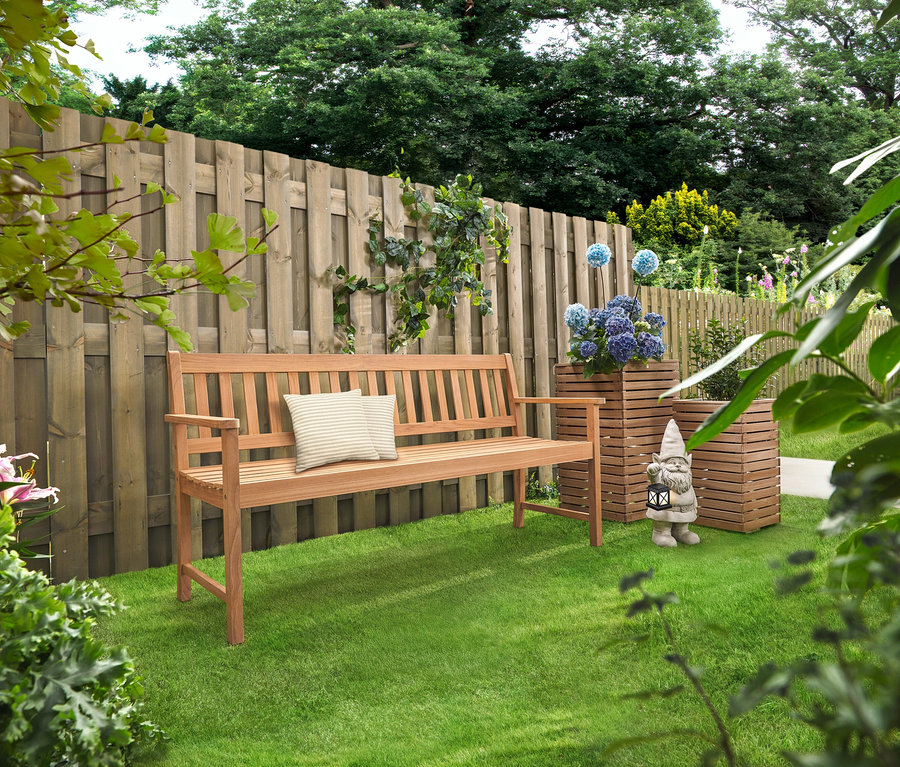 Egy fa pad párnákkal áll a füvön. Mögötte két »Tinus« virágoszlop áll kék virágokkal.