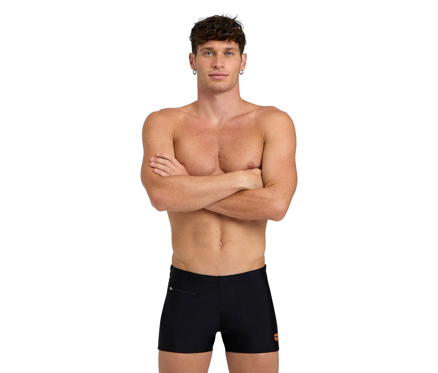 Férfi keresztbe tett karokkal, fekete fürdőnadrágban.