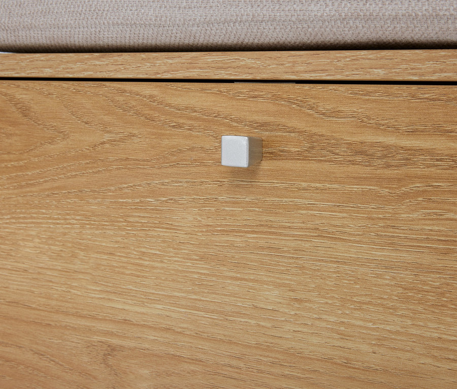 Egy világosbarna fa komód közeli képe fiókkal és ezüstszínű, négyzet alakú fogantyúval.