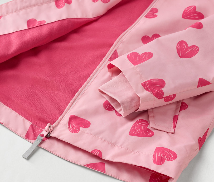 Egy kivilágosított, rózsaszín, piros szívecskés mintázatú, teljes hosszában cipzáras gyerekdzseki közeli képe.