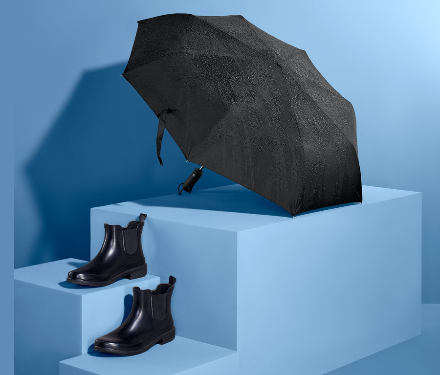 Fekete automata táskaernyő kék talapzaton, egy pár fekete cipő mellett.