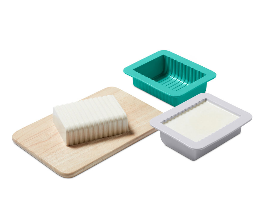 Egy tömb növényi vaj egy fa deszkán, egy zöld és egy szürke forma mellett a növényi vaj készítő készletből.