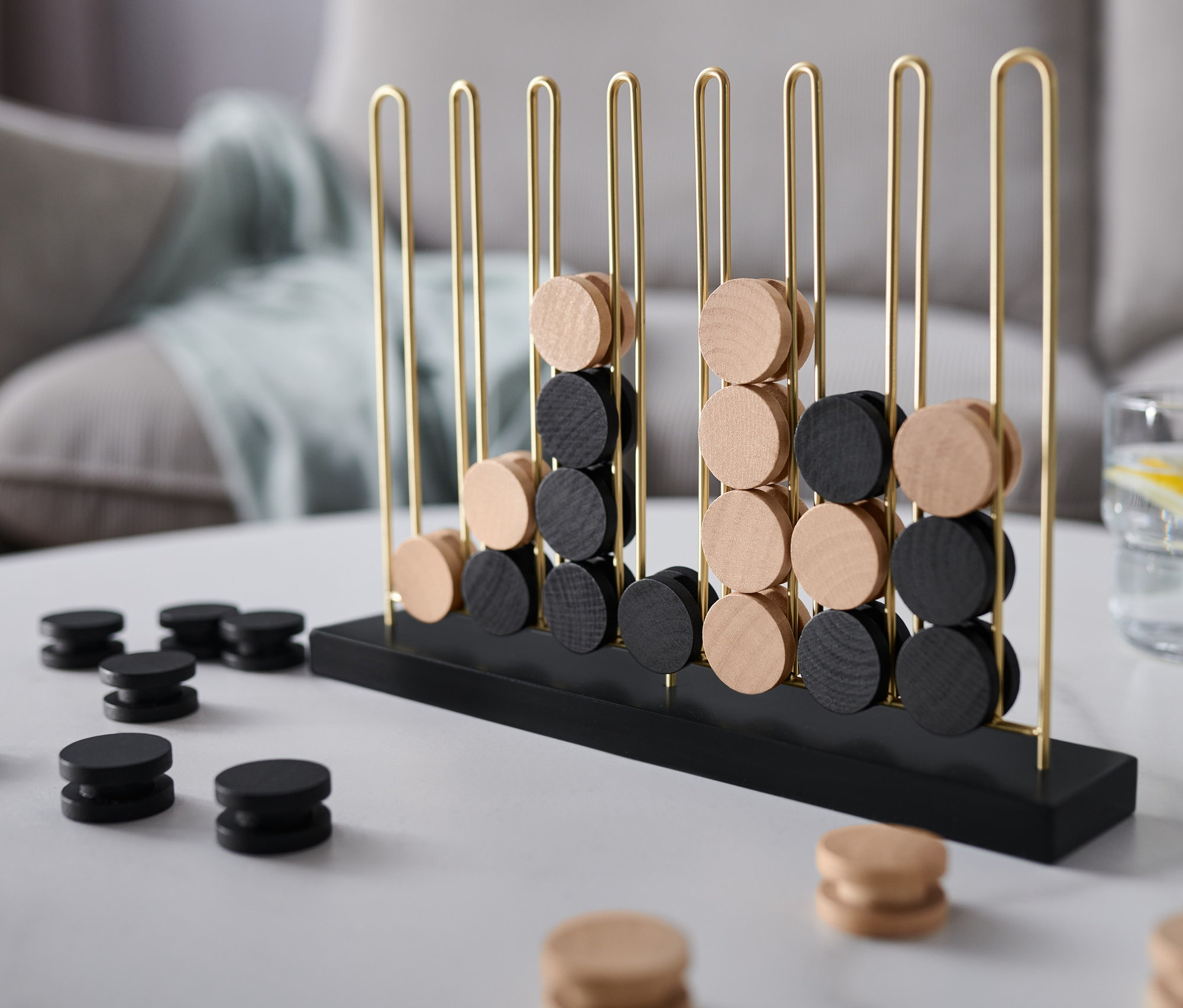 Amőba logikai játék fekete és világos fa korongokkal egy fehér asztalon.