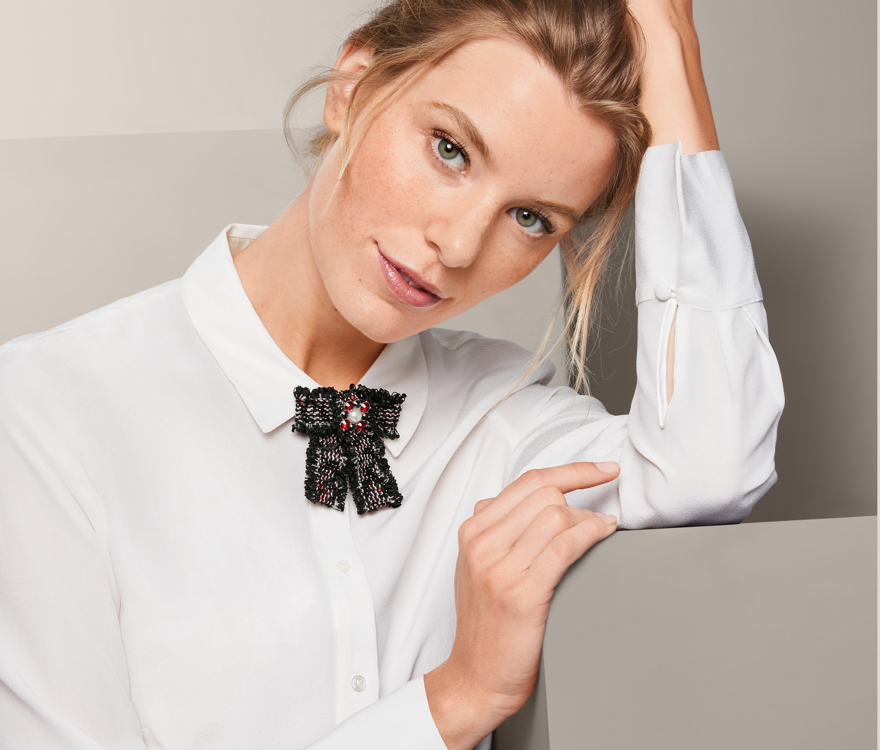 Nő tweed masni alakú brossal egy fehér ingben.