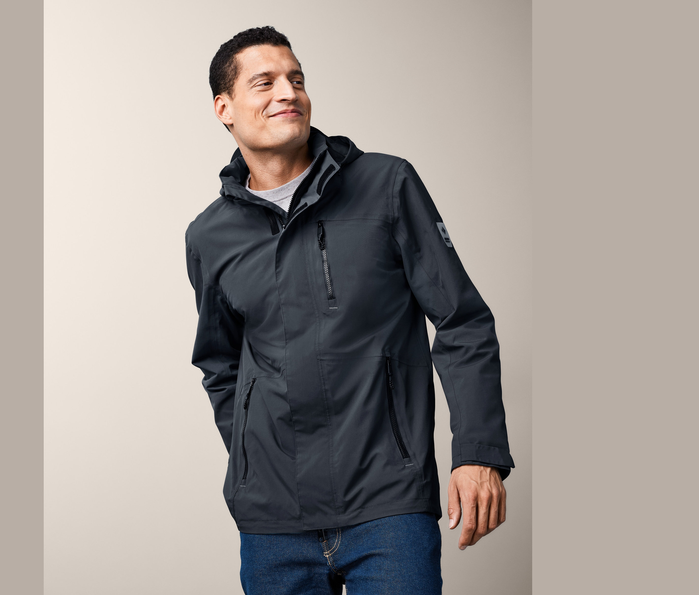 Mosolygó férfi sötétszürke funkcionális parkában és kék farmerben pózol.