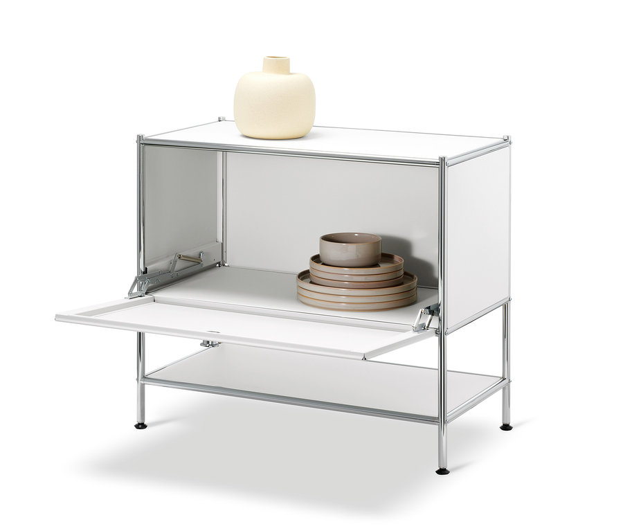 Fehér »CN3« komód nyitott ajtóval. A tetején egy bézs váza, a szekrényben tányérok és tálak találhatók.