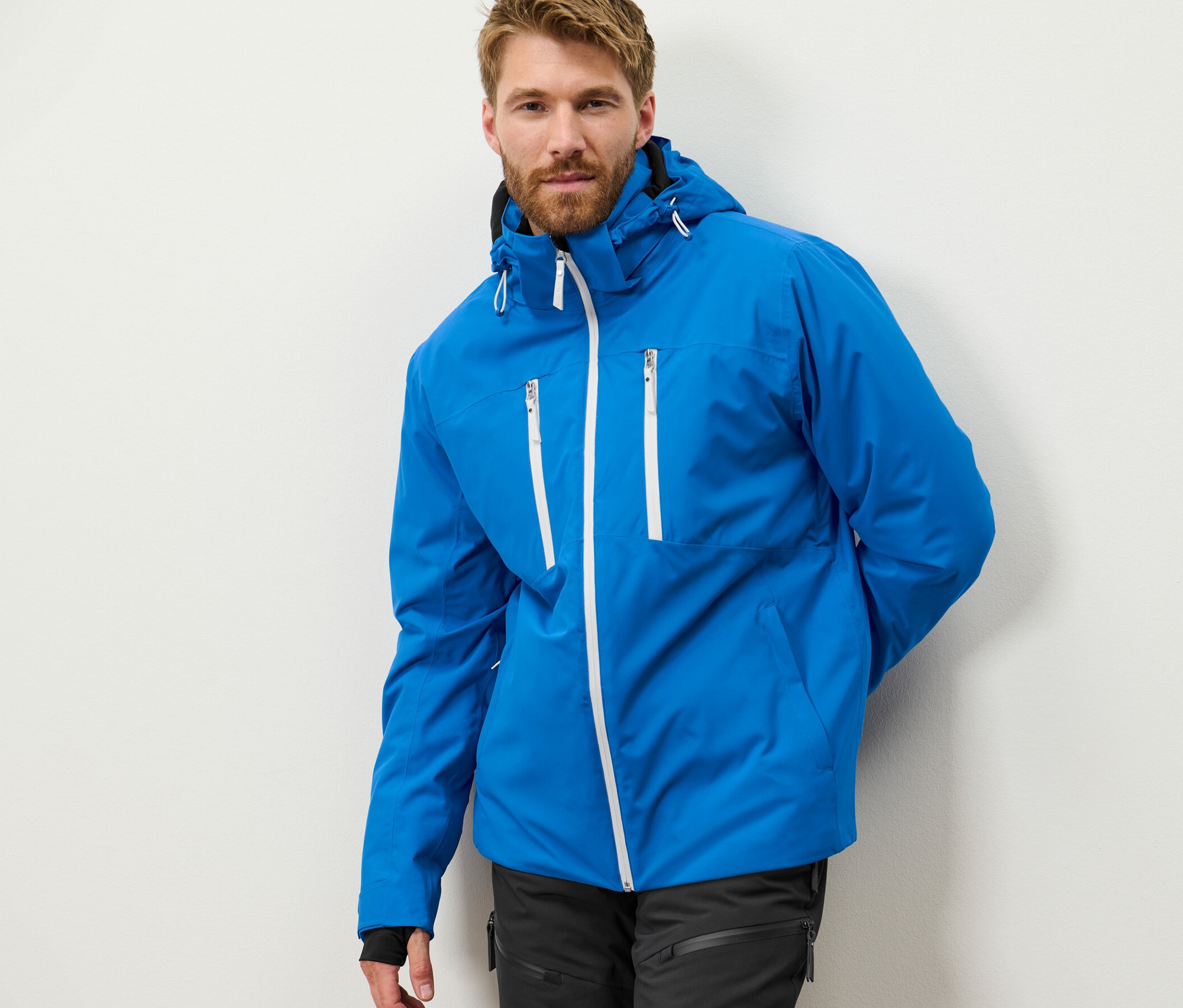 Szakállas férfi pózol kék, high-tech síkabátban.