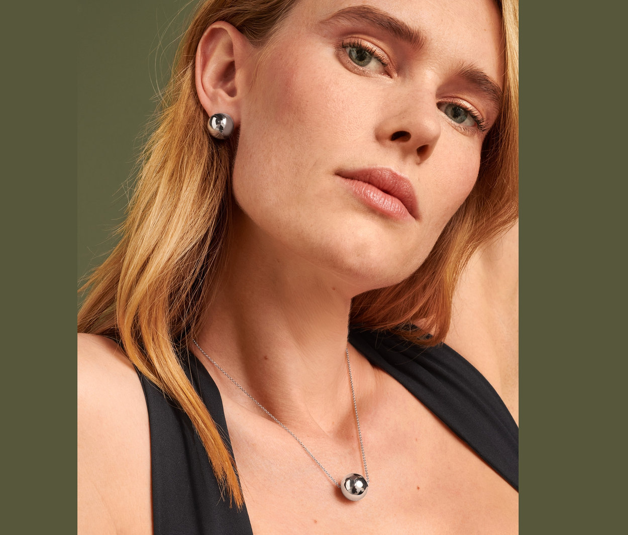 Szőke nő Fülbevaló Globe-ot és Nyaklánc Globe-ot visel.