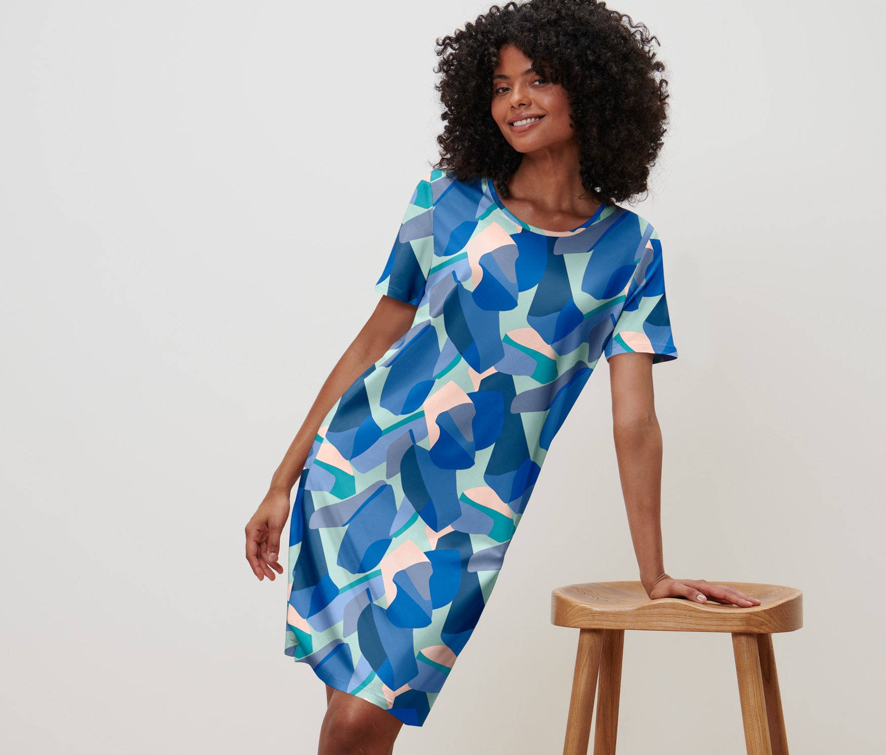 Nő pózol kék, mintás női hálóingben, és egy fa székre támaszkodik.