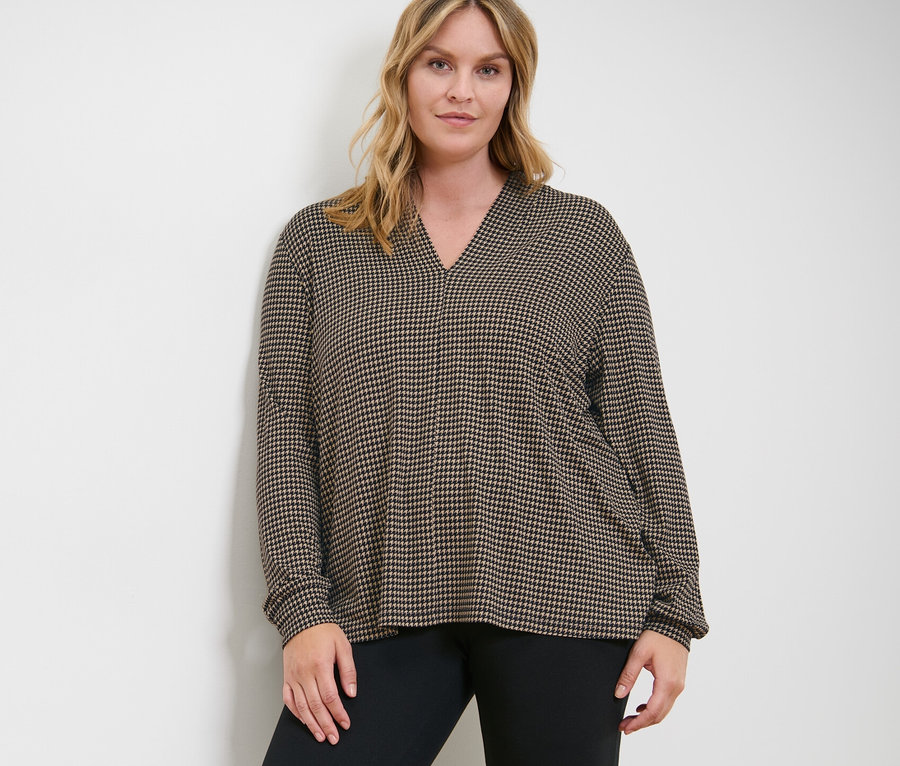 Nő pózol nyomott mintás pólóblúzban V-nyakkivágással és fekete leggingsben.