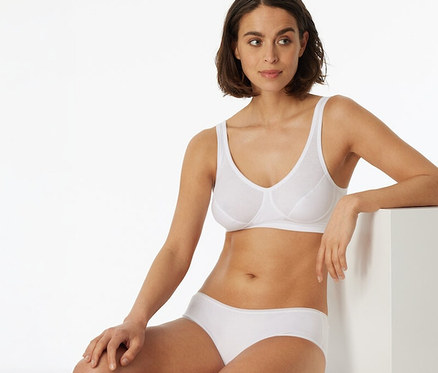Nő ül és fehér, 2 darabos SCHIESSER kosaras bustier melltartót visel biopamuttal.