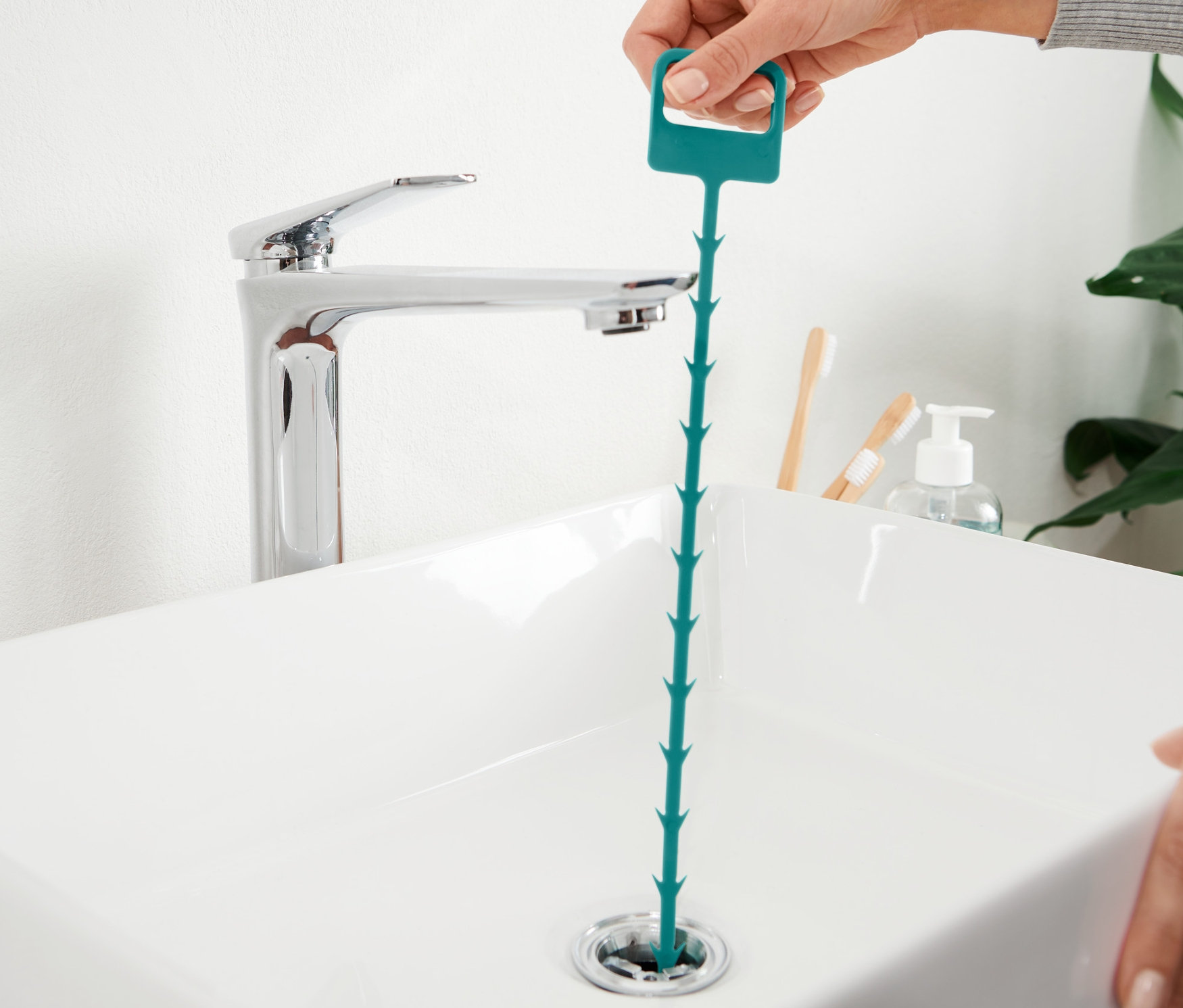 Egy kéz egy lefolyótisztítót helyez a mosogató lefolyójába.