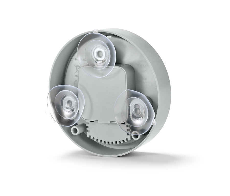 Közelkép egy fürdőszobai falióra hátuljáról, három átlátszó tapadókoronggal.