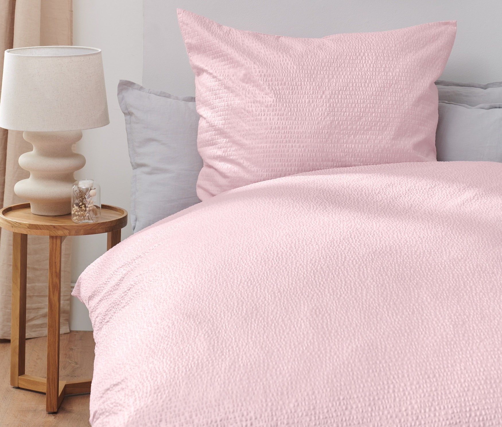 Rózsaszín krepp ágynemű egy ágyon, mellette egy faasztal lámpával.