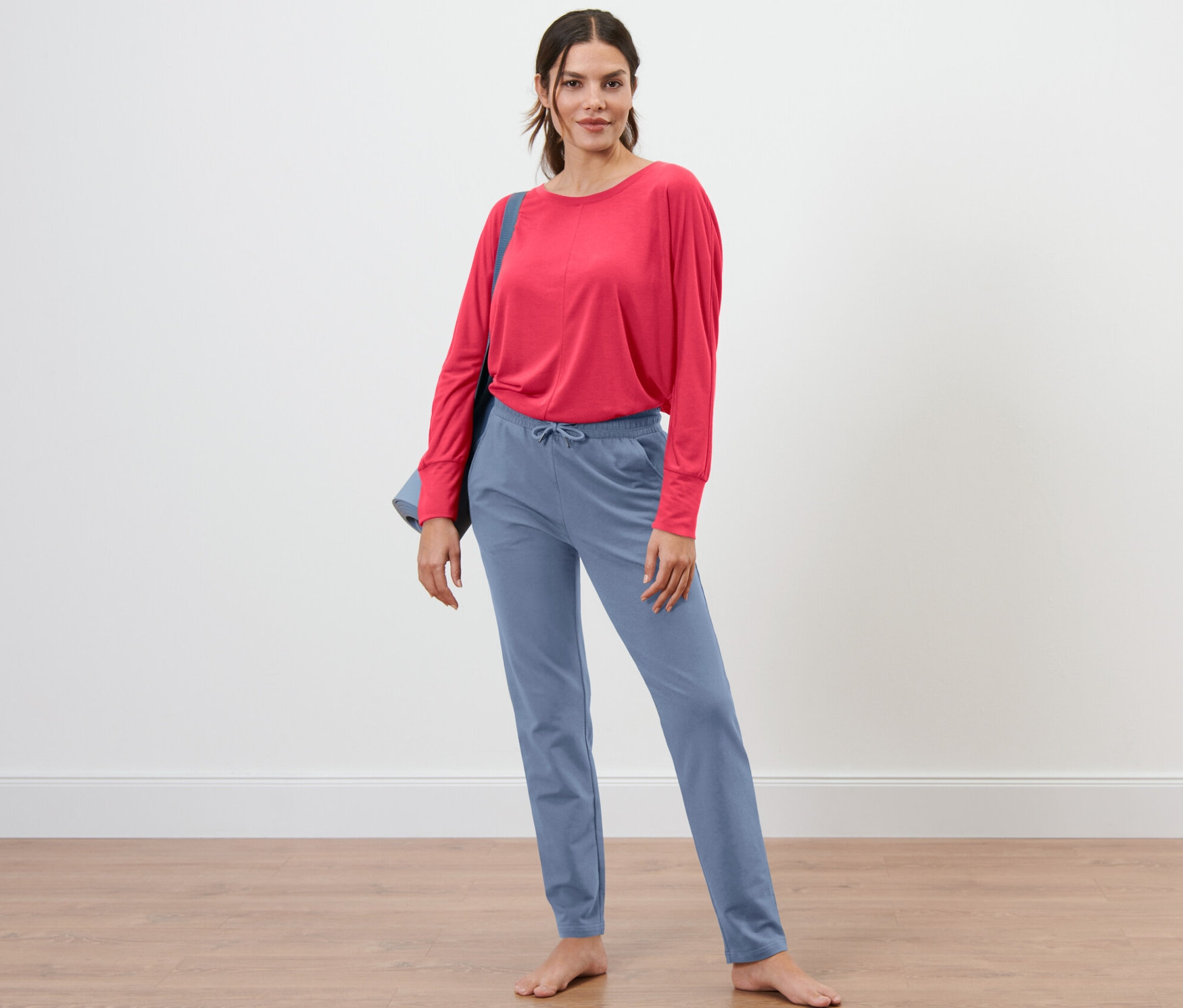 Egy nő áll mezítláb, kék szabadidőnadrágot és piros felsőt visel.