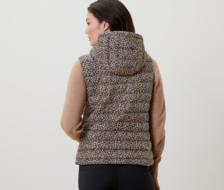 Hátulról látható nő nyomott mintás, kapucnis steppelt mellényt visel.