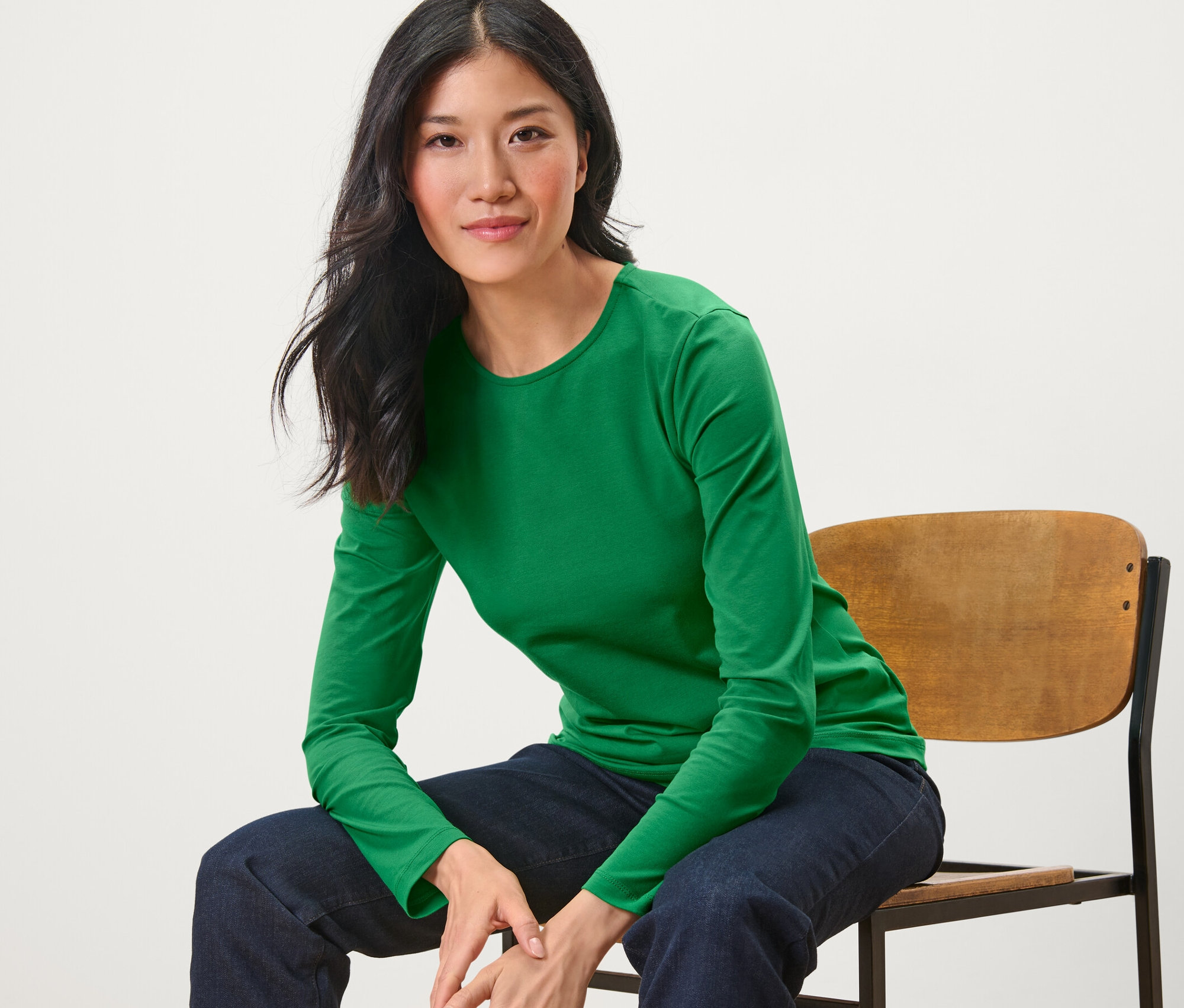 Nő ül egy széken, zöld hosszú ujjú felsőt visel.