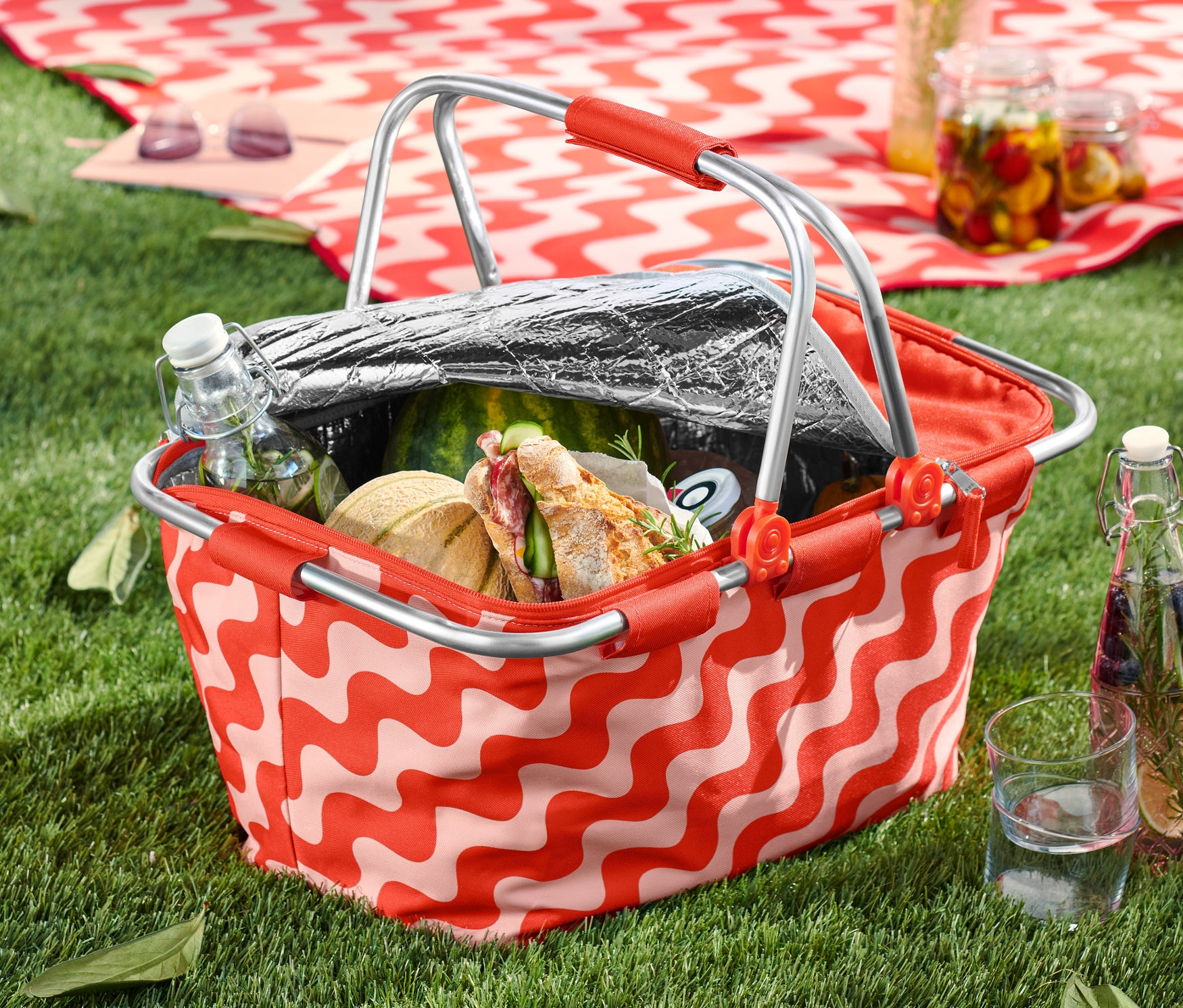 Egy mintás, összehajtható hűtőkosár tele étellel-itallal a füvön.
