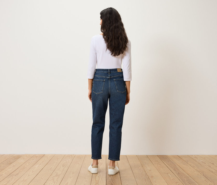 Hátulnézet egy sötét hajú nőről, aki kék farmert, fehér pólót és fehér cipőt visel.