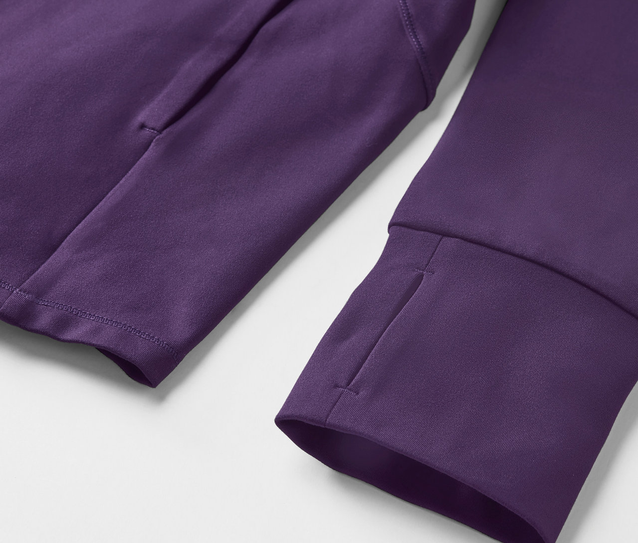 Egy lila, hosszú ujjú pulóver részlete, hüvelykujjlyukakkal és zsebbel a karon.