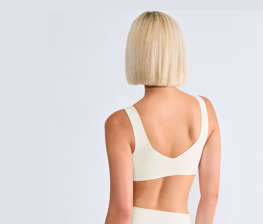 Hátulnézet egy szőke hajú nőről, aki selyemfehér sloggi ZERO Feel 2.0 bralette-et visel.