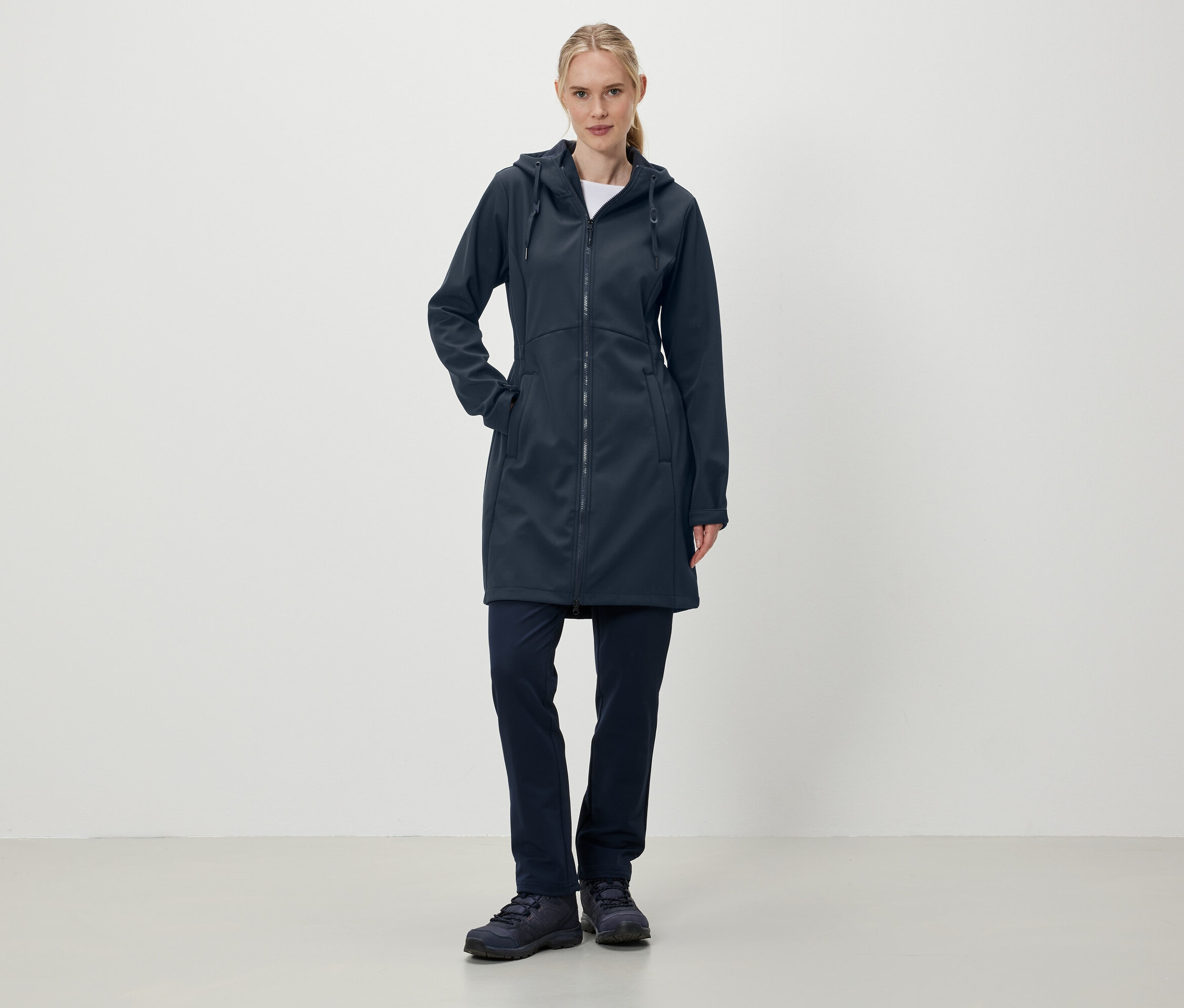Egy nő áll sötétkék kapucnis kabátban, nadrágban és cipőben.
