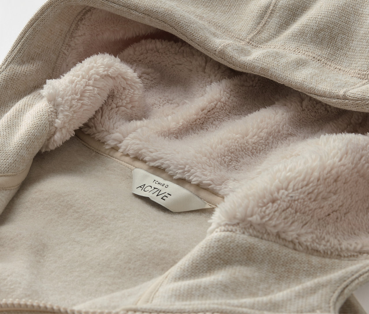 Egy bézs színű, fleece bélésű kapucnis pulóver részlete, ACTIVE címkével.