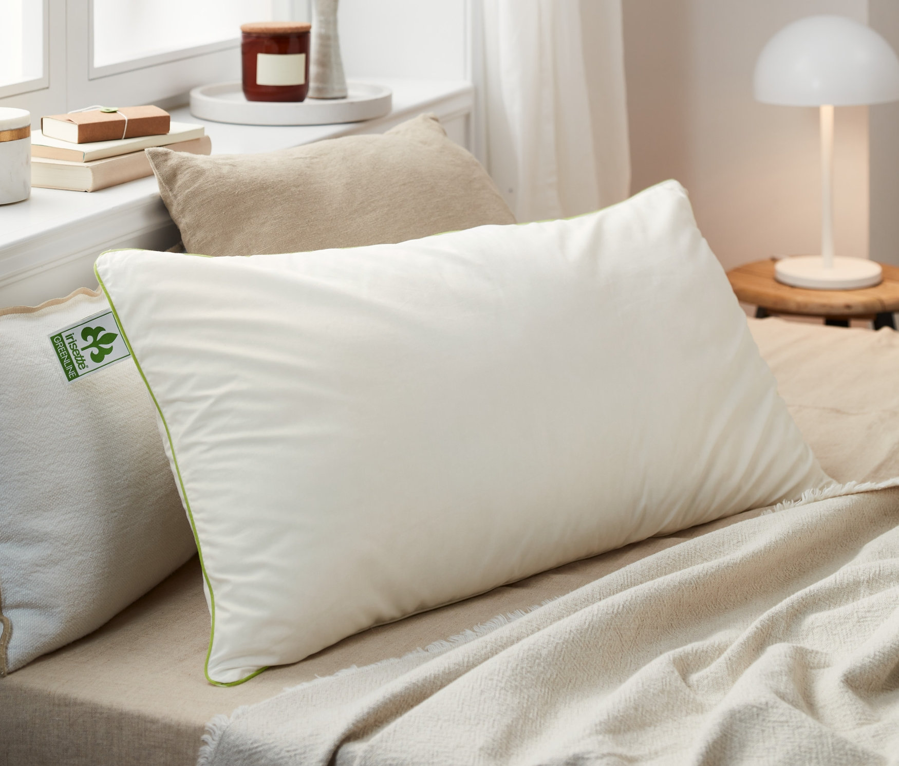 Több különböző méretű irisette® greenline tollpárna fekszik egy ágyon.