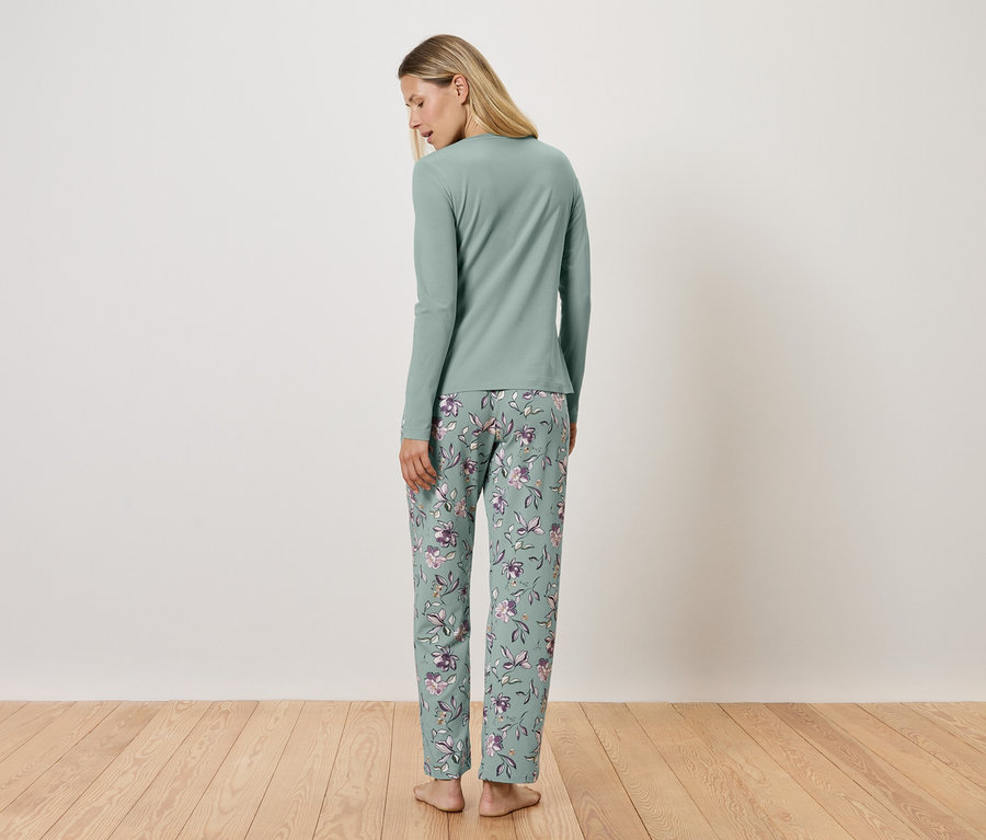 Egy nő áll háttal a kamerának, világoszöld, hosszú ujjú pizsamában és virágos nadrágban.