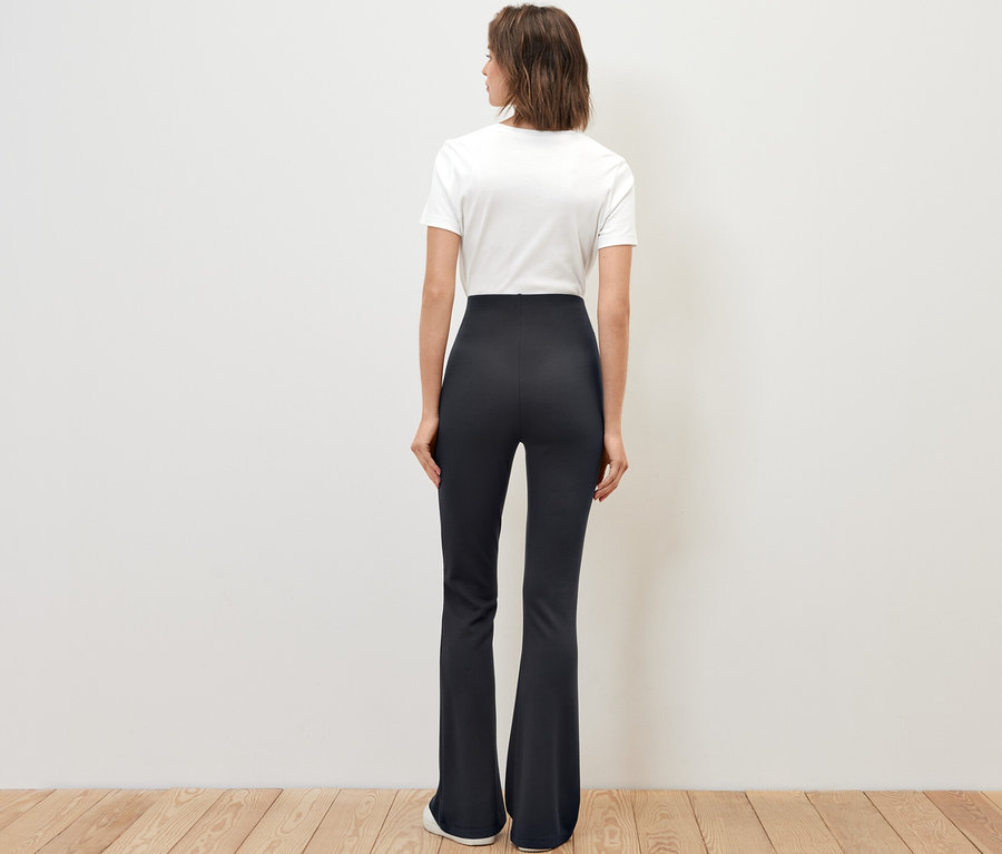 Nő áll háttal a kamerának, sötétkék, bőszárú legginget visel.