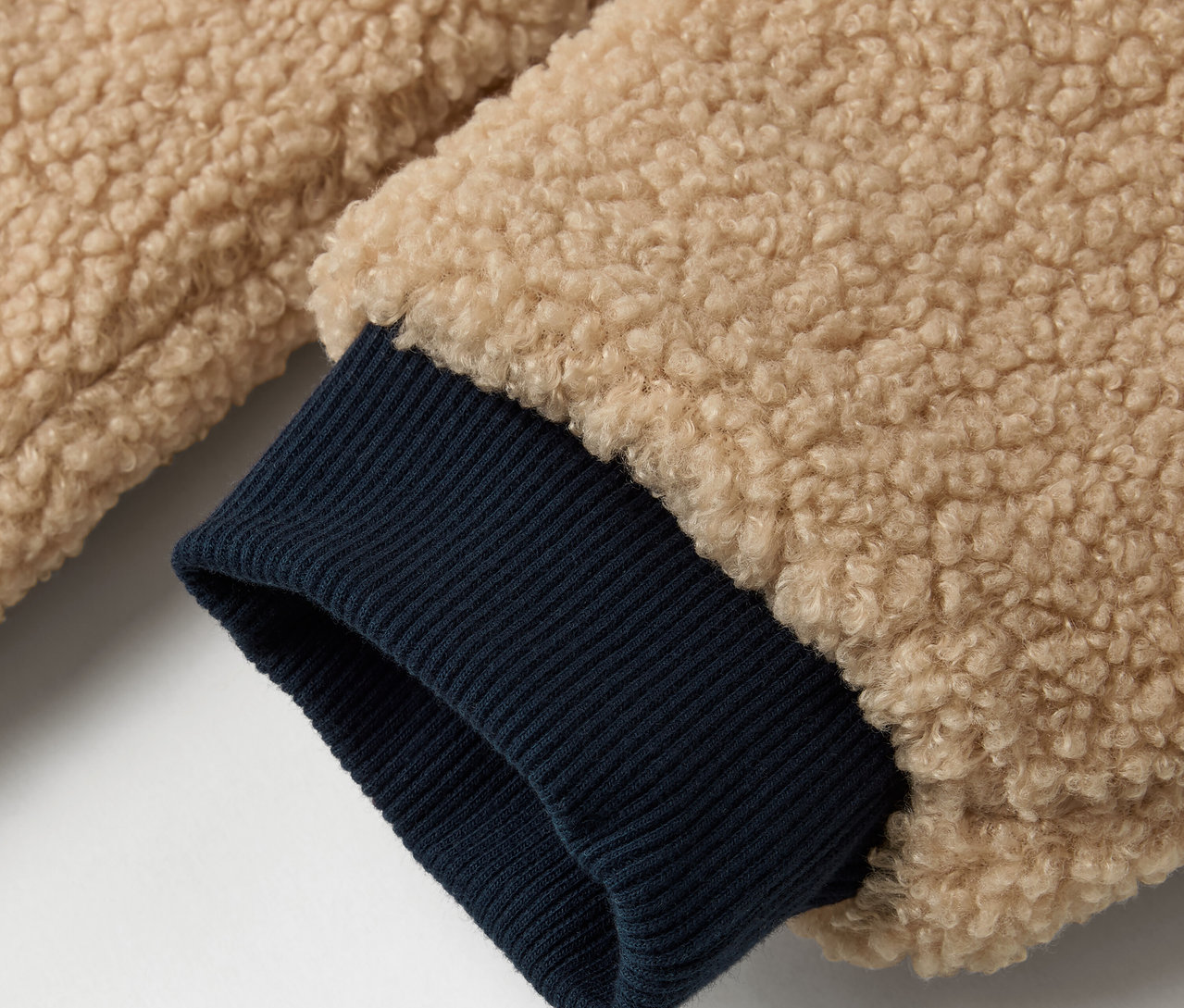 Egy bézs színű külsővel és sötétkék ujjú szegéllyel rendelkező Kinder-Wendejacke részlete.