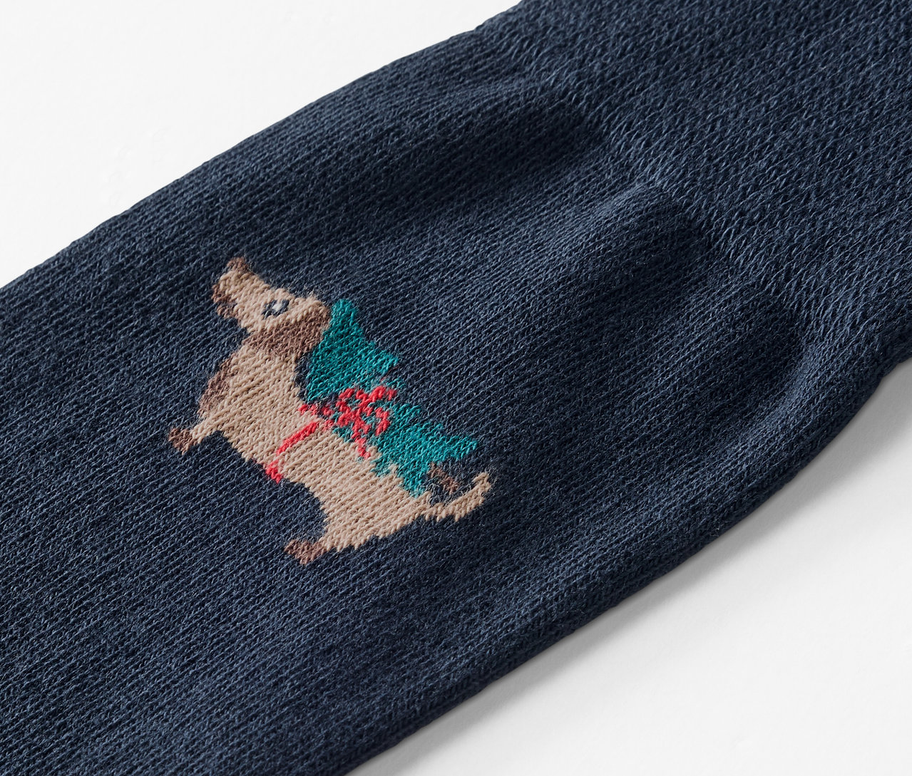 Egy kék zokni részlete, melyen egy karácsonyfát cipelő sün hímzése látható.