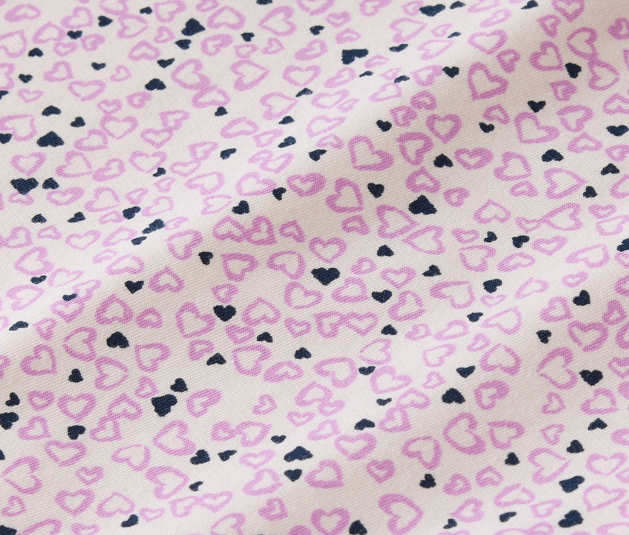 Közeli kép egy fehér alapon apró rózsaszín és sötétkék szívekkel nyomott szövetről.