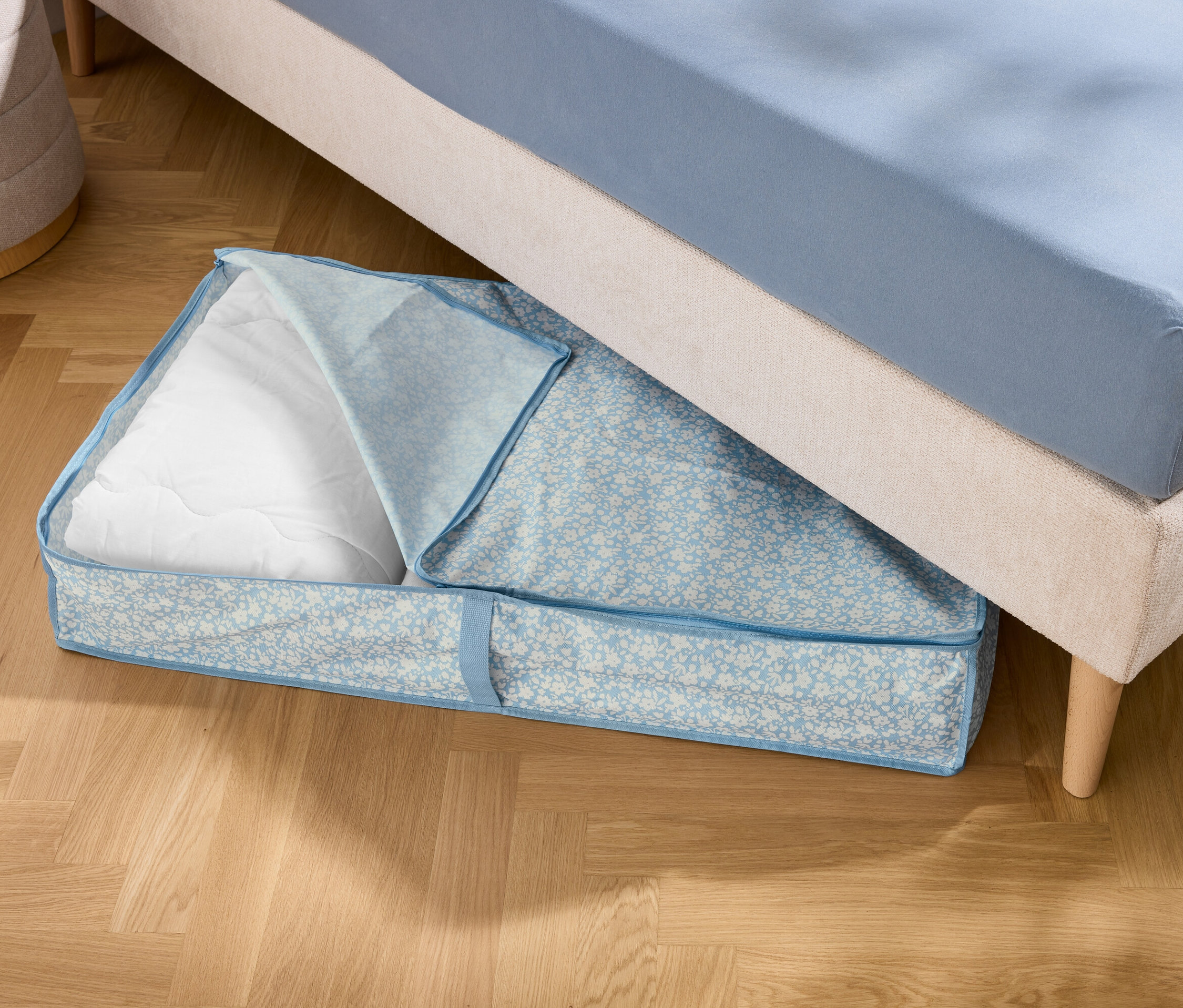 Egy ágy alatt egy kék tárolótáska fekszik fehér töltelékkel.