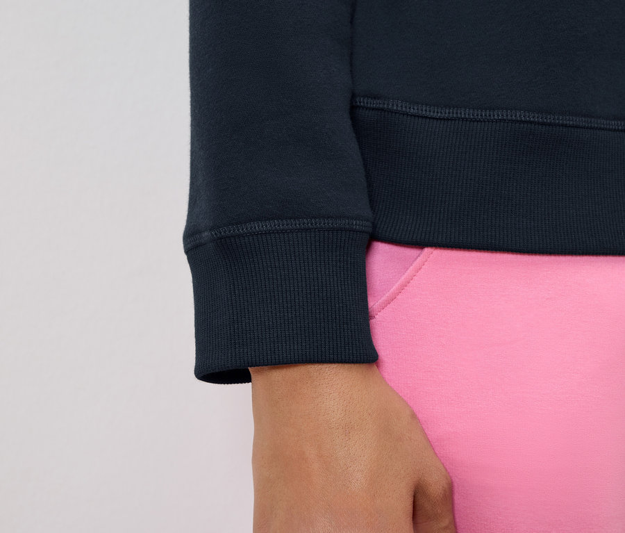 Egy sötétkék pulóver ujjának és egy rózsaszín nadrág egy részletének a képe.