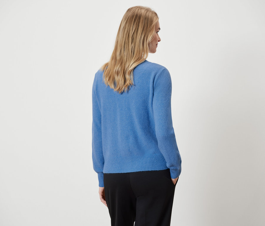 A képen hátulról látható egy nő, aki kék pulóvert és fekete nadrágot visel.