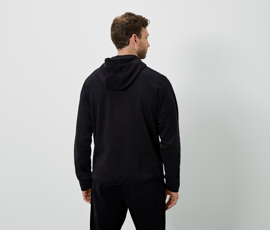 Egy férfi hátulról látható, fekete kapucnis pulóvert és fekete melegítőnadrágot visel.