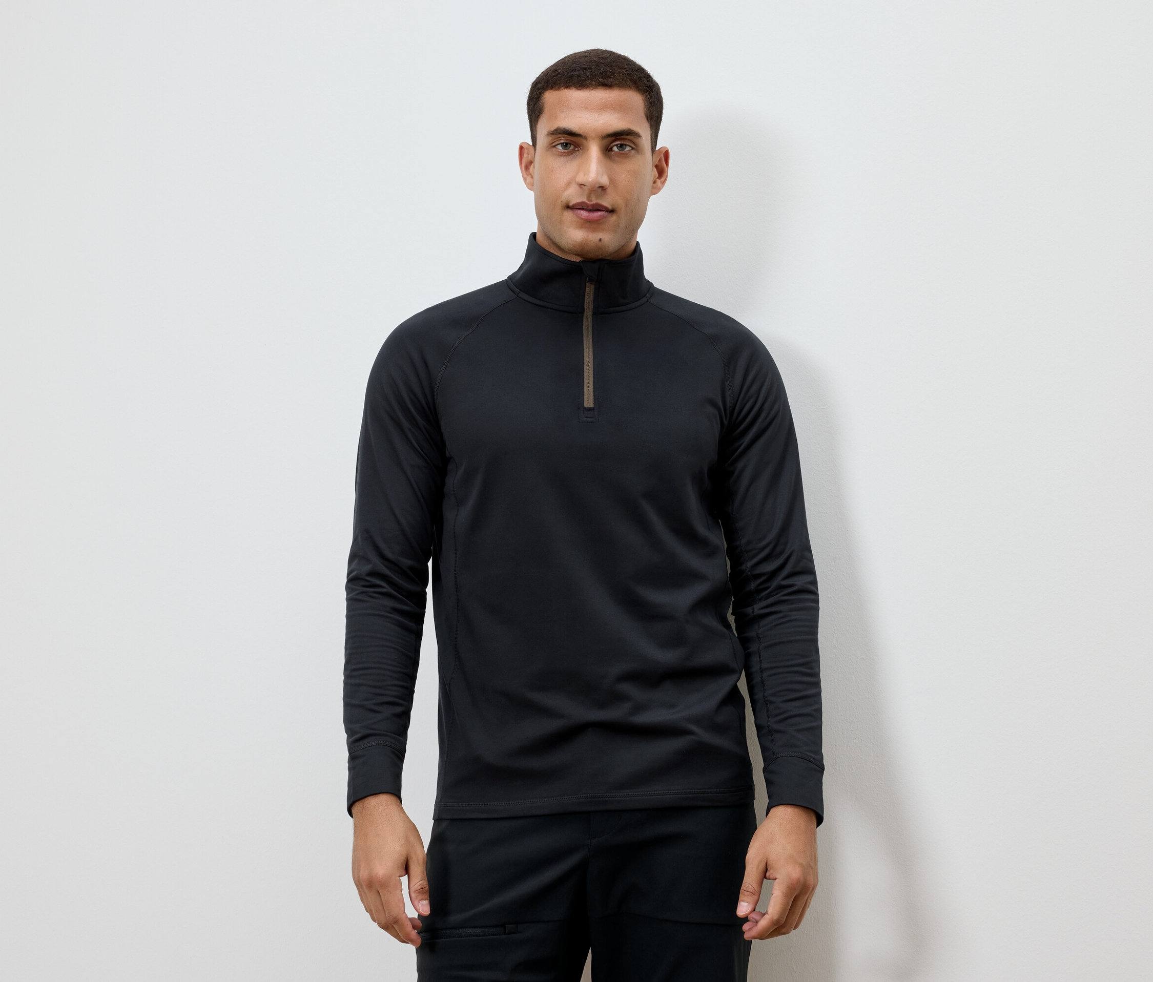 Férfi fekete, hosszú ujjú, cipzáras nyakú pólót visel.