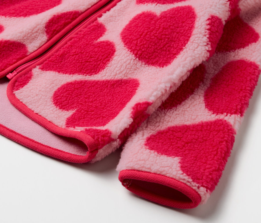 Egy rózsaszín, piros szív mintás fleece pulóver részlete.