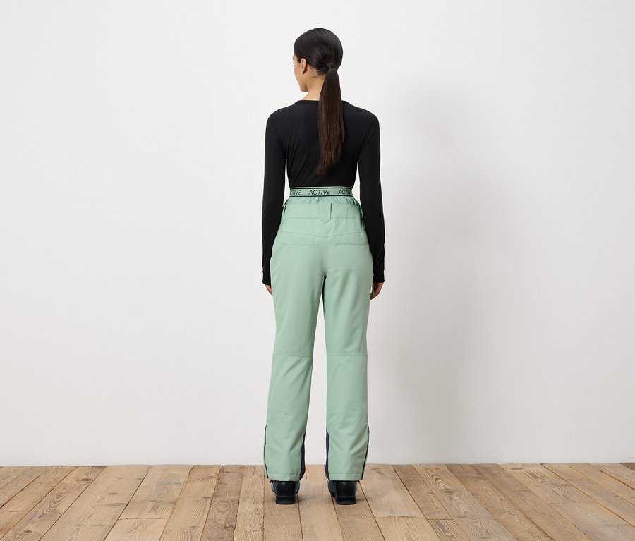 Egy nő háttal a kamerának, fekete hosszú ujjú inget és világoszöld nadrágot visel.