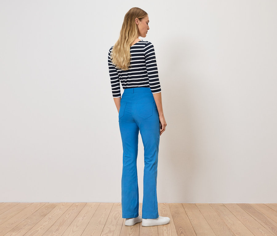 Egy nő áll háttal, kék nadrágot és csíkos pólót visel.