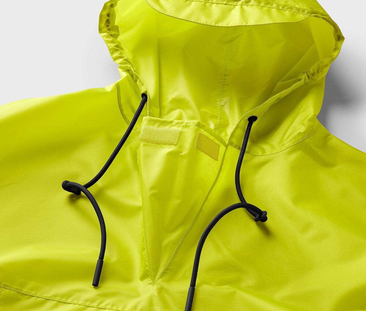 Egy neonsárga esőponcsó közeli képe kapucnival és fekete húzózsinórokkal.